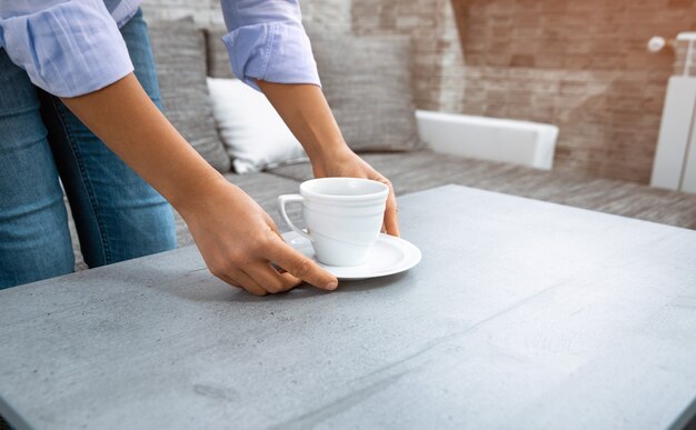 La vista delle mani di una donna che mette una tazza di caffè sul tavolo.