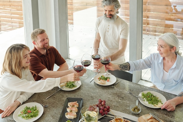 Above view of happy senior parents and their older kids clinking wineglasses during family dinner