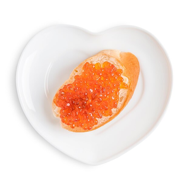 Photo above view of heart shaped plate with toast made of butter and red salmon fish caviar on white