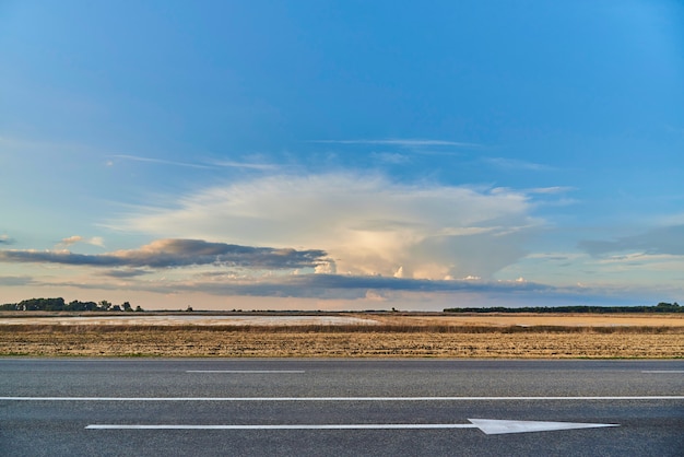 Photo view of the highway with arrow the forward and sunset in the field.