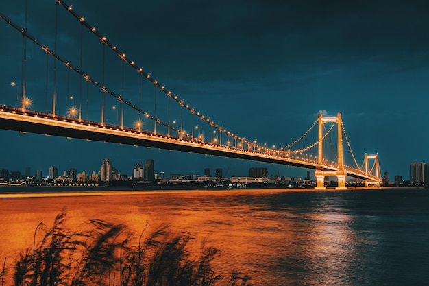 view of illuminated suspension bridge over river at night