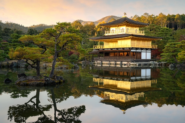 京都の秋のシーズンに日本庭園と劇的な夕方の空と池がある有名な金閣の金閣寺の景色。