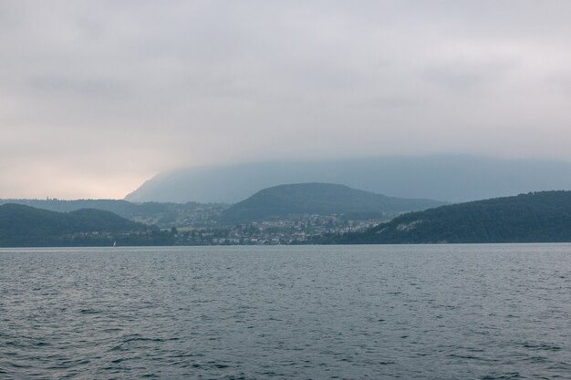 Вид на озеро Тун и горы с корабля в городе Шпиц, Швейцария, Европа. Летний пейзаж. Драматическая сцена с голубыми облаками