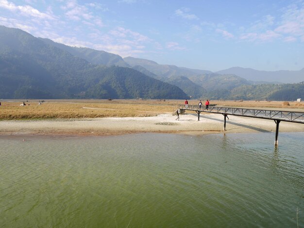 View landscape rice paddy field and nepali people walking on wooden bridge cross irrigation reservoir dam countryside rural and himalaya mountain at Pokhara hill valley village city in Pokhara Nepal