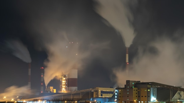 View of a large factory or plant in the light of night lighting A lot of smoke comes out of the factory's chimneys Pollution of the environment fire at a waste recycling plant