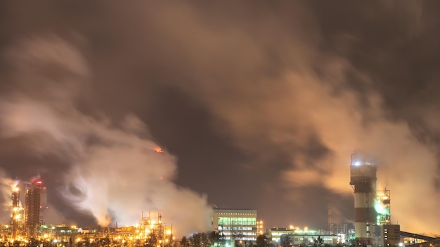 View of a large factory or plant in the light of night lighting A lot of smoke comes out of the factory's chimneys Pollution of the environment Toxic bad ecology