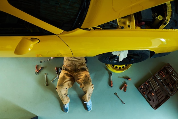 Above view of legs of mechanic or repairman fixing details of car