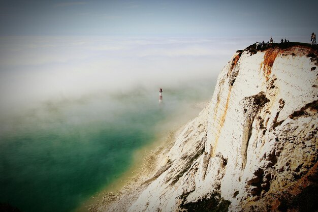 Foto vista del faro nella nebbia e delle persone su una scogliera contro un cielo nuvoloso