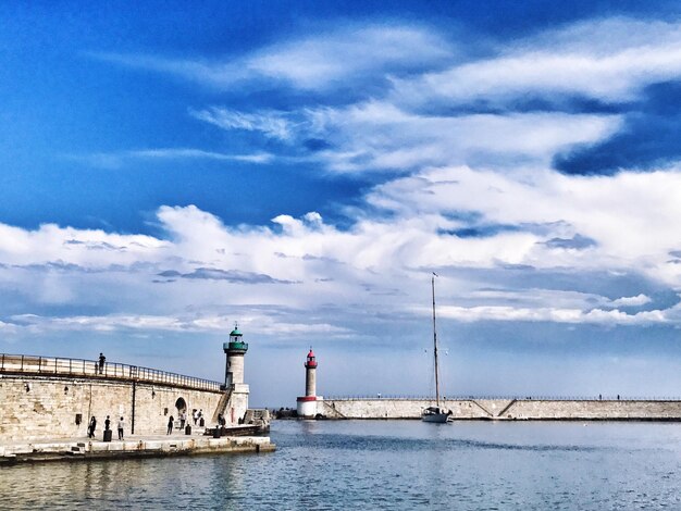 View of lighthouse in sea against cloudy sky