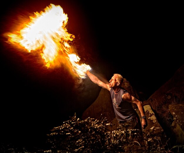 Photo view of man blowing fire at night outdoors