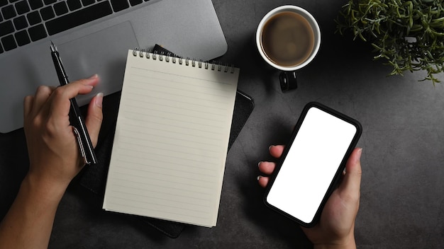 Above view man hand holding mobile phone and making notes on notebook