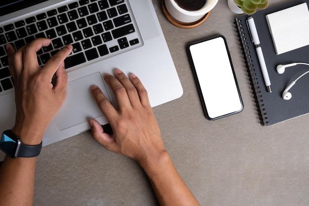 Above view of man hands typing on laptop at office desk with smart phone coffee cup and notebook