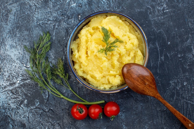 Sopra la vista di purè di patate servito con pomodori freschi con cucchiaio di legno di aneto su sfondo di colore scuro con spazio libero