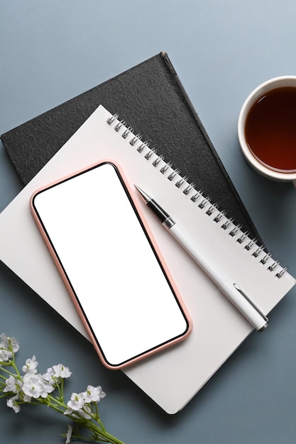 Above view of mobile phone with empty screen and notebook on blue table