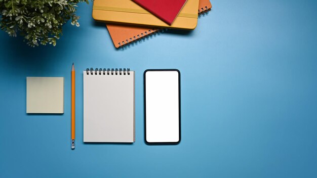 Above view mockup smart phone notepad and sticky note on blue background