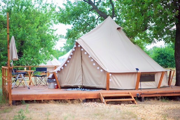 View of modern camping tents in the glamping area. Camping tent with all the amenities. Civilization in the forest. Tent with light and furniture