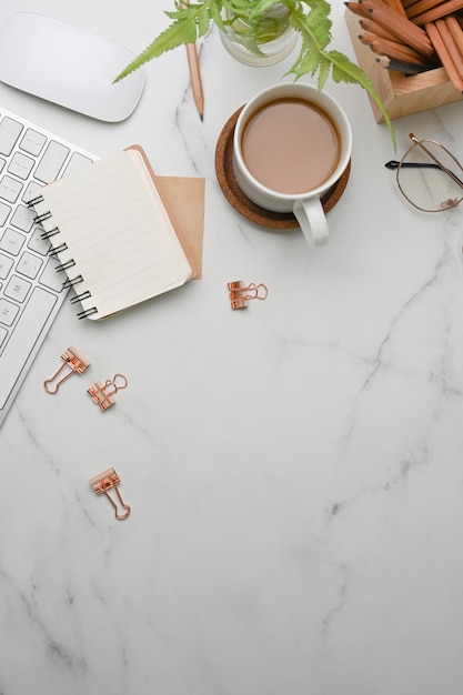 Above view of modern workplace with notebook, glasses, coffee cup and copy space on marble background.