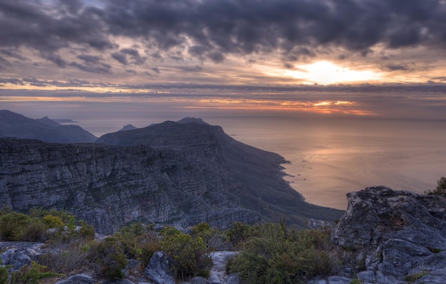 Above view of a mountain coastline at sunset in South Africa Scenic landscape of dark clouds over a calm and peaceful ocean near Cape Town with the sun behind grey clouds in the sky and copy space