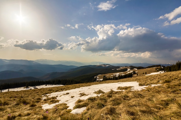 View of mountain valley with dry grass and spots of snow, distant mountain range stretching to horizon on sunny blue sky copy space background.