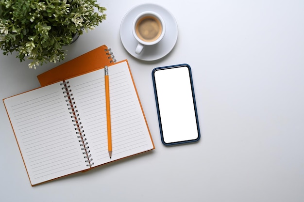 Above view of office desk with smart phone, notebook, keyboard, coffee cup and notebook on white background.