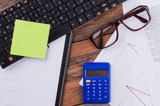 Above view of office workplace with glasses documents keyboard blue calculator