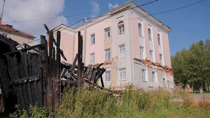 Фотография вид на старый заброшенный дом с упавшей гипсовой клип зеленой травой и старым сожженным деревянным зданием