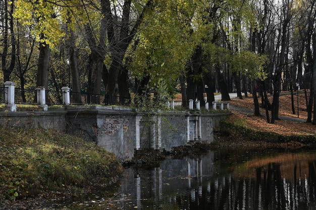 Вид на старый мост через пруд. Пруд и старые большие деревья. Осенний день.