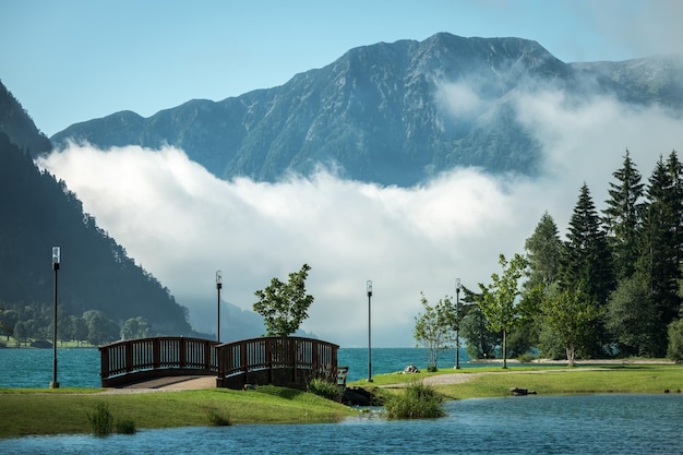 View of park with wooden bridge over river and trees on grass by mountains