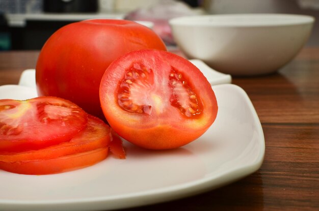 View of part of a white plate with slices and half of fresh red\
tomato with side view