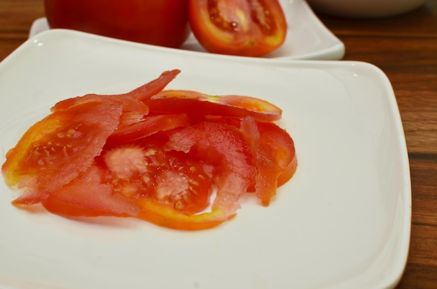 Вид на часть белой тарелки с ломтиками и половину свежего красного помидора с видом сбоку.