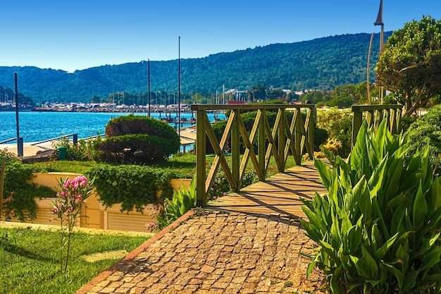 View of the path and the bridge in a green garden with green trees along the embankment in kemer tur