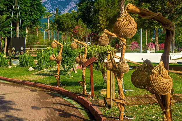 View of the path and wooden lanterns along the path in a green garden with green trees along the embankment in Kemer