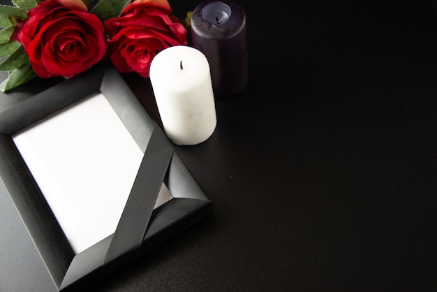 Above view of picture frame with red flowers and candles on dark surface