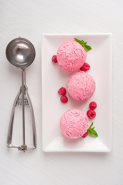 Above view of pink refreshing berry ice cream scoops on plate with raspberries and mint leaves