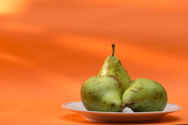 Photo view of a plate with three conferencetype pears set on an orange background