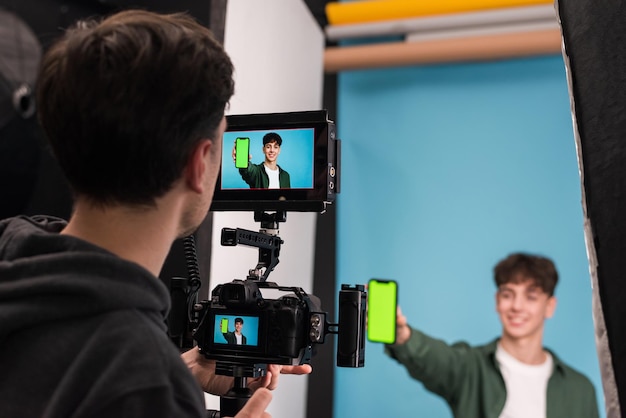 Вид профессионального фотографа, снимающего молодого человека, показывающего смартфон с зеленым экраном