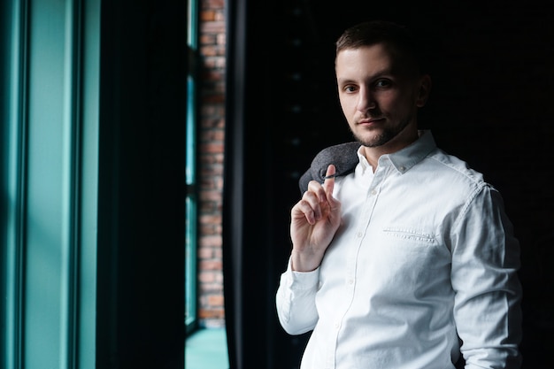 View in profile of a young businessman, dressed in a white shirt standing near the window 