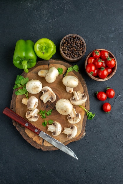 Выше вид сырых грибов и зелени, нож на деревянной доске, белое полотенце и свежие овощи на черном фоне