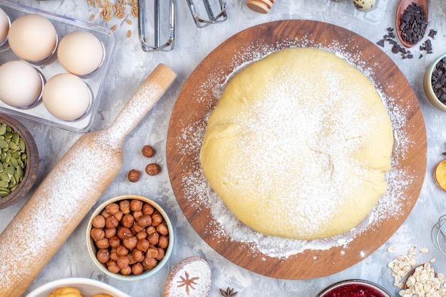 Above view of raw pastry on round wooden board grater and set of foods on ice background