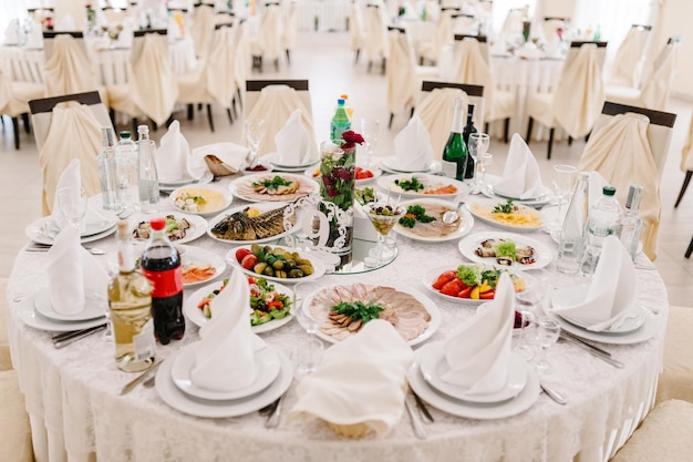 レストランホールの眺め結婚式の宴会場のお祝いテーブルテーブルクロスで覆われたゲストテーブルお祝いテーブルで夕食を提供フードサラダ肉魚の食事