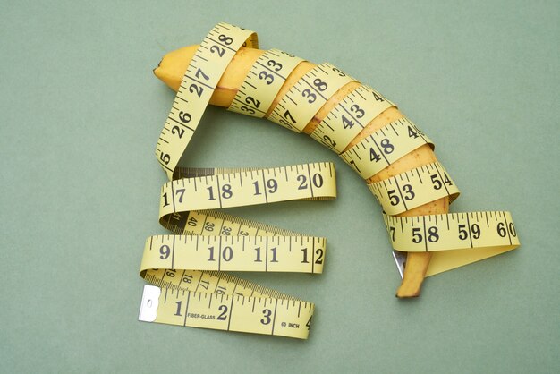 Above view of ripe banana wrapped into tape measure against green background