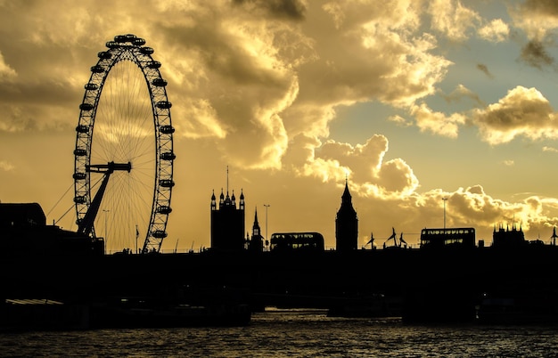View of river by ferris wheel in city against cloudy sky