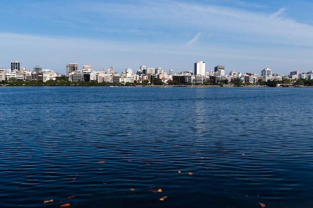 Photo view of rodrigo de freitas lagoon south zone of rio de janeiro brazil in the background dois irmaos hill and pedra da gavea sunny day buildings around pond water used for sports