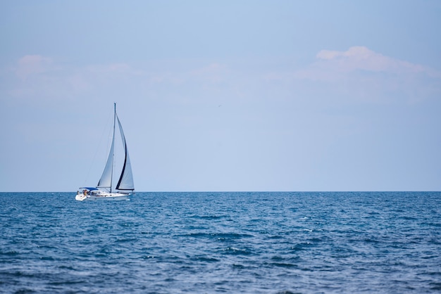 A view of the sea, a white yacht with sails and the sky.