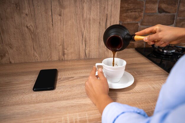 The view over the shoulder of a woman pouring coffee from a Turkish coffee.