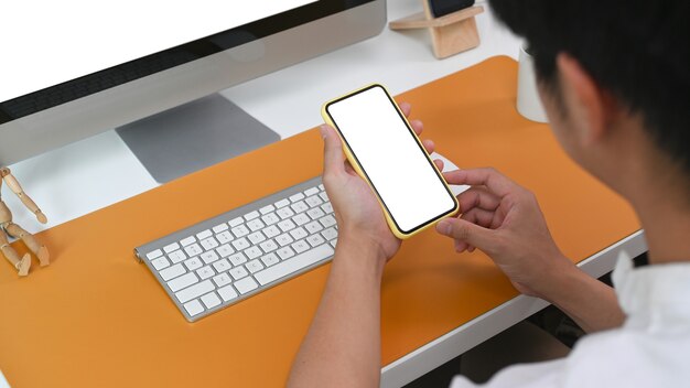 View over shoulder young man sitting in office and using smart phone.