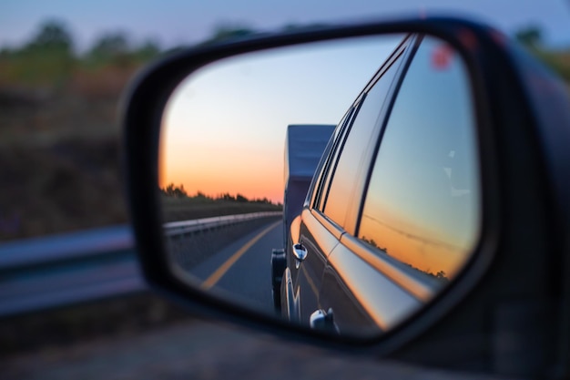 View in the side mirror of a moving car on a caravan and a sunset in the sky