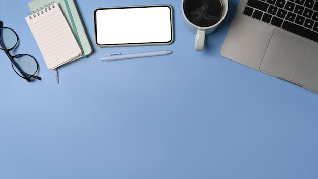 Above view smart phone, laptop computer, notebook and coffee cup on blue background.