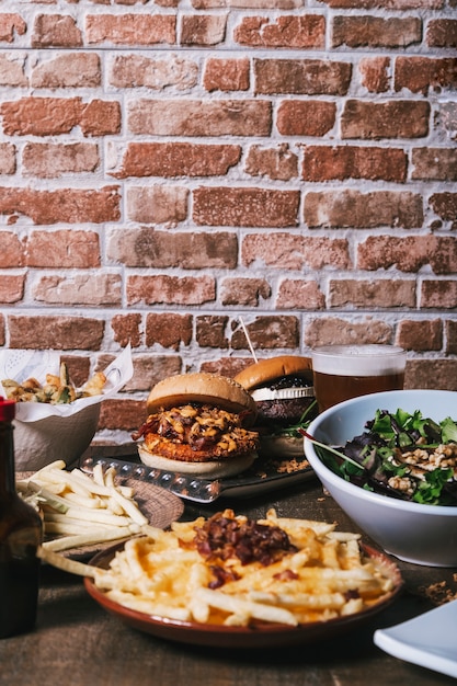 View of the table with a variety of dishes, hamburgers, french fries and salad, drinks and sauce on the wooden table. Restaurant menu. Vertical image