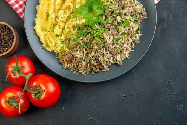 プレートに肉のマッシュポテトとトマトの茎が落ちたオイルボトルペッパーと黒の背景に空きスペースがあるおいしいディナーのビューの上